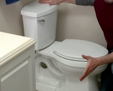 A man demonstrates a white dual-flush ceramic toilet installation in a bathroom.