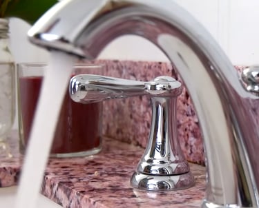 Polished chrome bathroom faucet running water over a pink granite countertop.