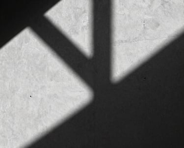A high-contrast black and white photograph of architectural shadows on a smooth concrete wall. Abstract and editorial.