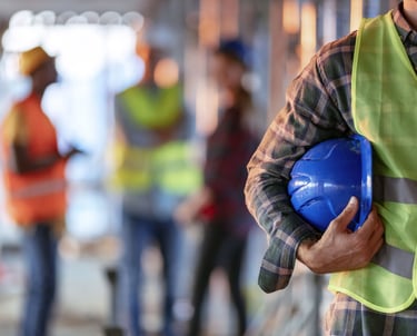 Man wearing a safety vest and holding a hard hat standing in front of other workers