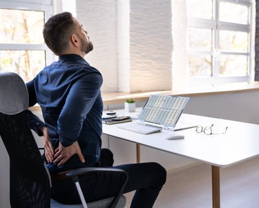 Man sitting at his desk holding his back in apparent pain