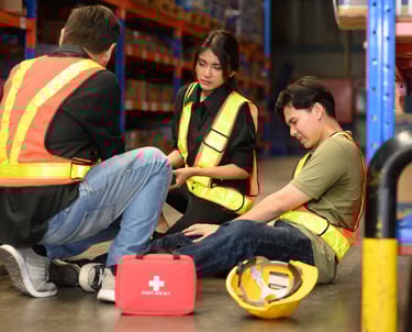 Man sitting on the ground at his workplace who has suffered an injury with coworkers assisting