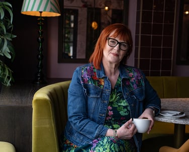 Dawn Vincent Celebrant sat on a velvet sofa with a coffee cup in hand