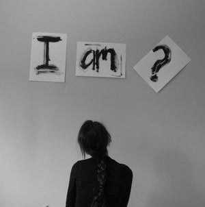 Person standing under “I am?” signs representing self-awareness, identity questioning