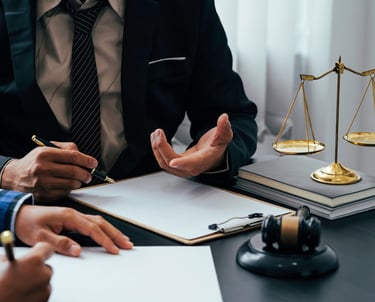 Professional lawyer in a suit providing legal advice to a client with a gavel and scales of justice on the desk.