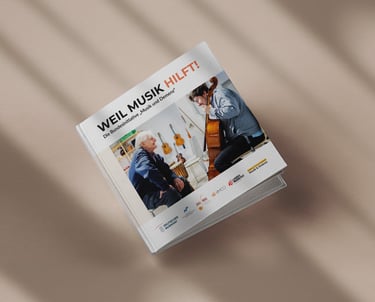 Gedruckte Broschüre „weil Musik hilft” liegt auf beigem Boden mit Schattierungen