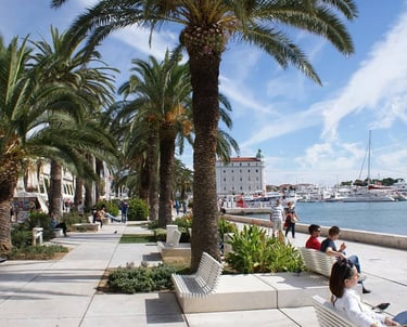 Palm-lined Riva promenade in Split with people walking and boats in the harbour