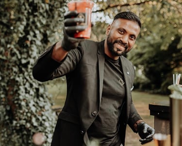 Professional mobile bartender in a black suit serving a fresh cocktail at an outdoor event.
