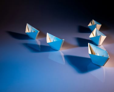 A strategic formation of paper boats arranged on a blue surface, led by one of them