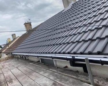 Newly installed black plastic guttering on a tiled residential roof with professional scaffolding.