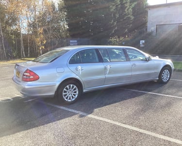 Silver Mercedes-Benz E-Class stretch limousine with white wedding ribbons parked in a sunny lot.