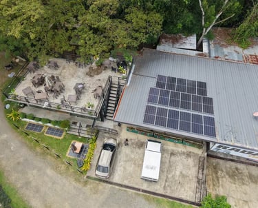 Aerial view of a restaurant with a rooftop patio, parked cars, and solar panels on a metal roof.
