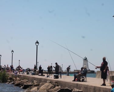 Anglers fishing on a concrete pier with a white lighthouse and lampposts under a clear blue sky.