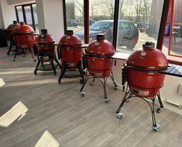 A row of red Kamado Joe ceramic grills on display in a modern outdoor cooking showroom.