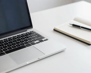 Detail photography of a professional office desk with a laptop and a notebook. Minimalist, clean, white and blue accents, professional vibes.