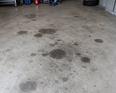 Dark oil stains and grease spots on a concrete garage floor near automotive tools.