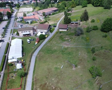 Aerial view of a rural equestrian center and farm buildings next to a grassy hill and paved road.