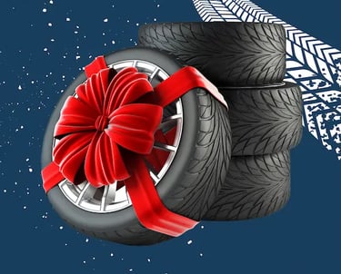 Cuatro neumáticos de coche apilados y un quinto neumático con una llanta plateada y un gran lazo de regalo rojo, todo sobre u