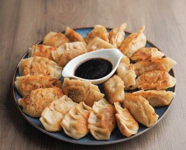 Gyozas grillés dorés servis par six avec une coupelle de sauce soja et des oignons verts.