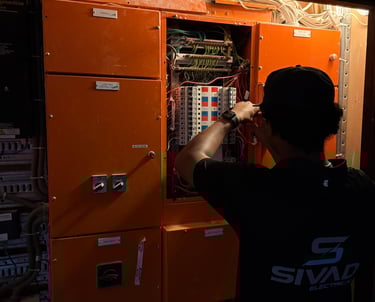 Professional electrician inspecting an orange industrial circuit breaker panel and electrical wiring.