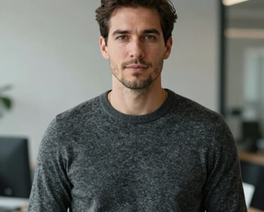 Professional portrait of a man in a modern charcoal grey sweater, looking approachable and professional, with a minimalist office interior blurred in the background. North American / International.