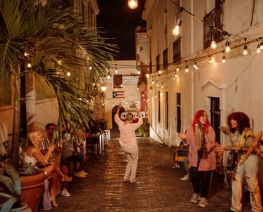 People dancing and playing music in a narrow Old San Juan street decorated with string lights at night.