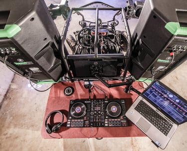 Professional DJ setup on wheels with a controller, laptop, headphones, and large speakers.