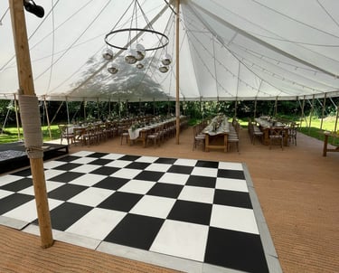Elegant outdoor wedding marquee with a checkered dance floor and rustic wooden banquet tables.