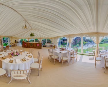 Elegant wedding marquee interior with draped ceiling, round dining tables, and chiavari chairs.