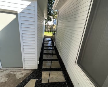 Narrow side yard path with modern concrete pavers and black lava rock mulch between white houses.