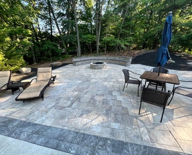 Custom stone paver patio featuring a round fire pit, curved stone bench, and outdoor dining furniture.