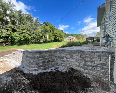 New gray stone retaining wall installed in a backyard landscape next to a residential house.
