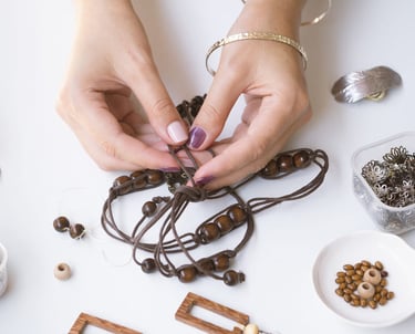 Diseñador de joyería artesanal ensartando un collar de cuentas de madera con cordón de cuero y dijes