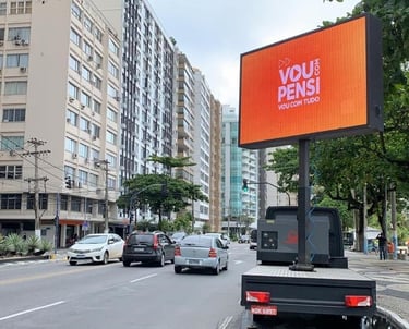 Digital LED billboard truck advertising on a busy city street near high-rise buildings and trees.
