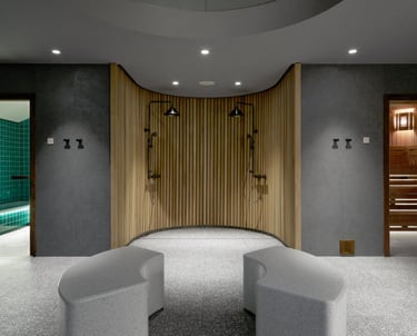 A bold, open-concept bathroom with dual showers, curved walls, lap pool, sauna, and central benches.
