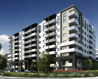 Nine-story apartment building in white and beige, featuring landscaped sidewalks with plants.