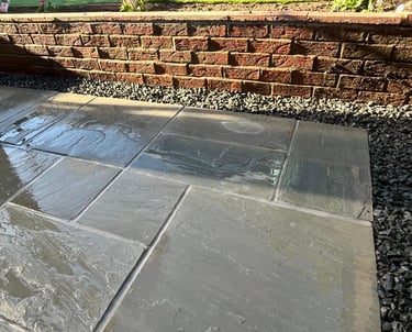 Wet grey flagstone patio tiles with black gravel borders and a red brick retaining wall.