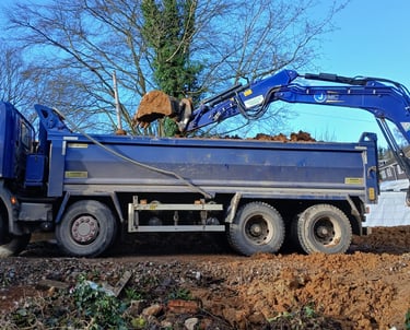 A blue grab lorry being loaded with soil by an excavator at a construction site.