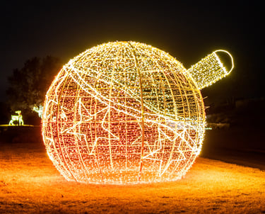 Large outdoor commercial Christmas ornament light display lit with warm gold and red LEDs at night.