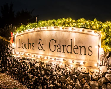 A stone sign with illuminated by warm white string lights at night, highlighting the entrance to a festive