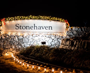 HOA community entrance sign, adorned with festive Christmas lights, at night.