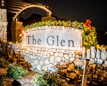 neighborhood stone entrance sign decorated with Christmas lights and festive holiday greenery at night.