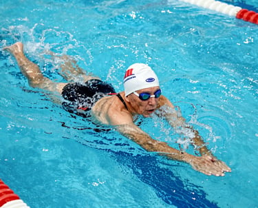 A group of smiling seniors participating in a gentle aquatic exercise session in a bright indoor pool.