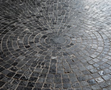 A detail of a circular mosaic floor in a minimalist entryway, using dark grey stones of varying textures, elegant and simple.