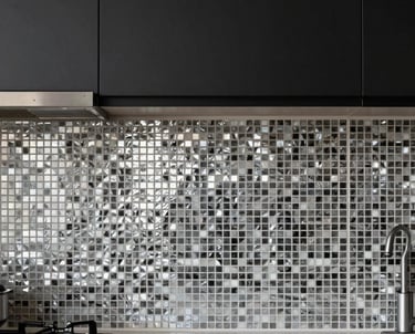 A modern kitchen with black cabinets and a backsplash made of small silver-toned mosaic tiles, reflecting soft kitchen lights.