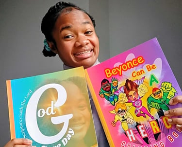 A smiling woman holds two colorful children's coloring books featuring inspirational and superhero themes.
