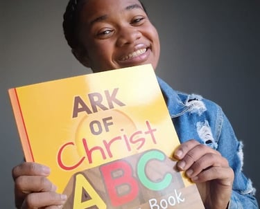 Smiling young girl holding up an Ark of Christ ABC Coloring Book for Children.