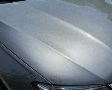 Close-up of a gray car hood showing visible swirl marks and paint scratches in the sunlight.