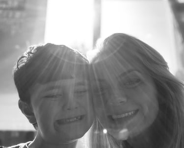 Black and white portrait of a smiling mother and son with bright sunlight creating lens flares.
