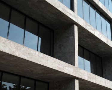 Exterior architectural photograph of a modern commercial building facade in Mexico / Latin America. Crisp geometric concrete beams, dark charcoal panels, and sleek glass reflections captured in bright daylight.